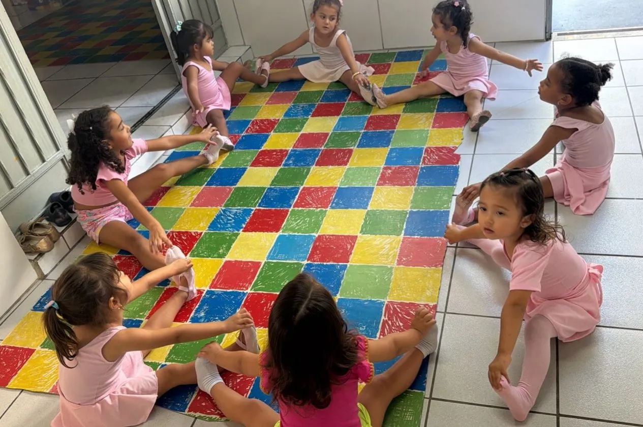Alunas da aula de balé fazendo alongamento em grupo no tatame colorido