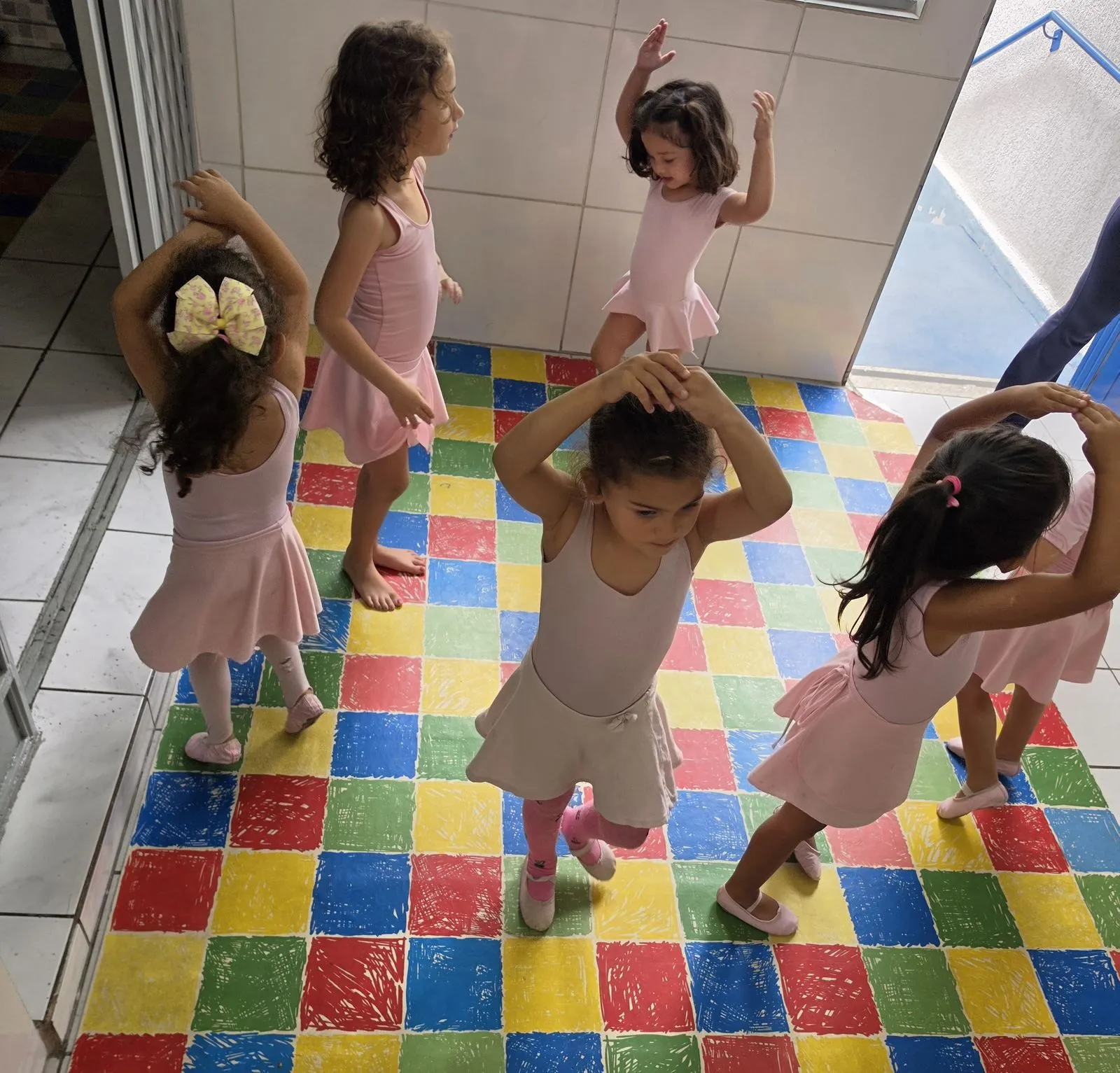 Turma da aula de balé em pé no tatame colorido, com os braços erguidos durante a atividade